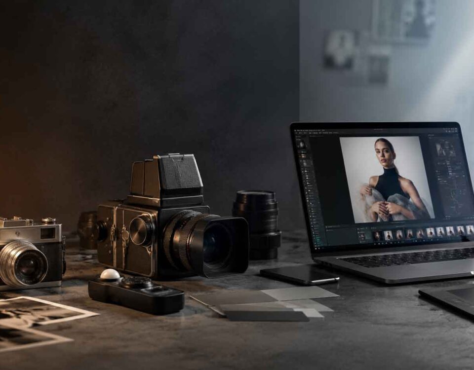 Birou de lucru creativ cu aparat foto analog, cameră profesională și laptop care afișează un portret editat, simbolizând trecerea de la fotografia clasică la producția vizuală AI.